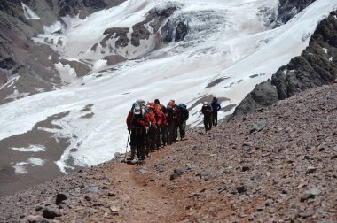 Karlı ve sarp dağlarda sıra sıra dağcıların aşırı koşullardaki hareketleri.