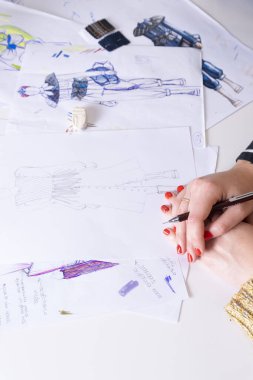 Genç esmer kadın renkli kalemlerle moda elbisesi tasarlıyor. Çeşitli renkli moda çizimleri ve çizimleri