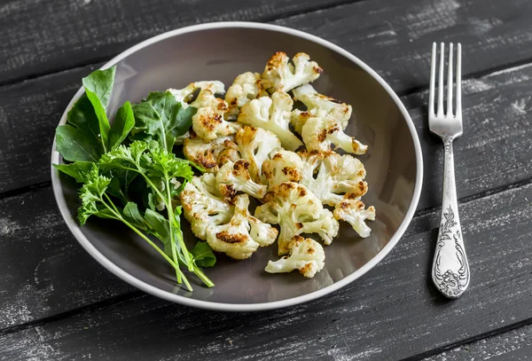 roasted cauliflower and fresh green salad on a brown plate on a dark wooden background