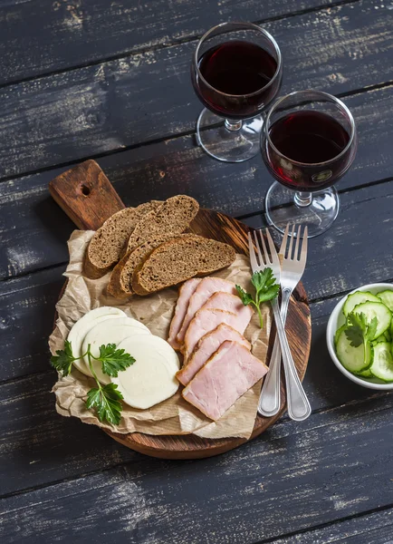 Delicious snack to wine. Smoked ham, cheese and two glasses with red wine on dark wooden background