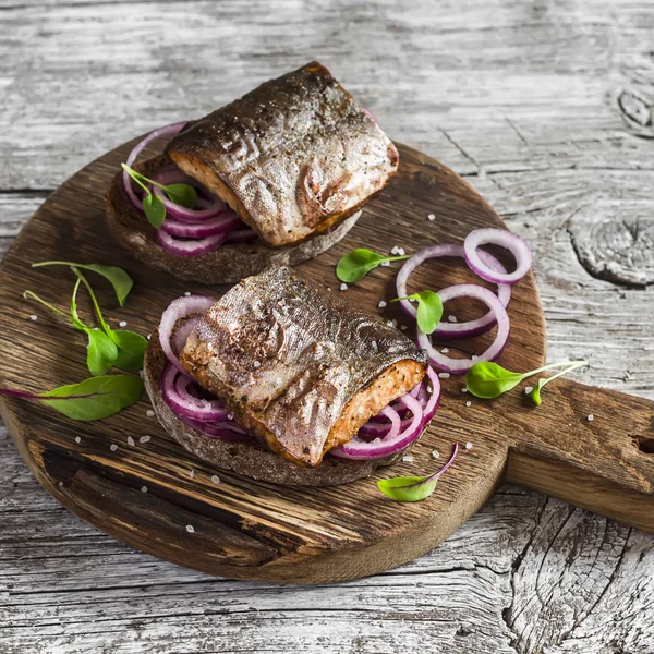 Sandwiches with grilled fish and quick pickled onions on rustic wooden board