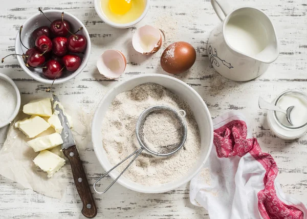 Baking rustic light background. Raw ingredients for baking pie with cherries - flour, eggs, milk, sugar, butter, cream, cherries.  Rustic style