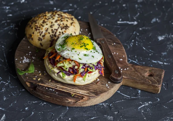 Homemade burger with fried egg and coleslaw on a rustic wooden board on a dark background. Healthy delicious food