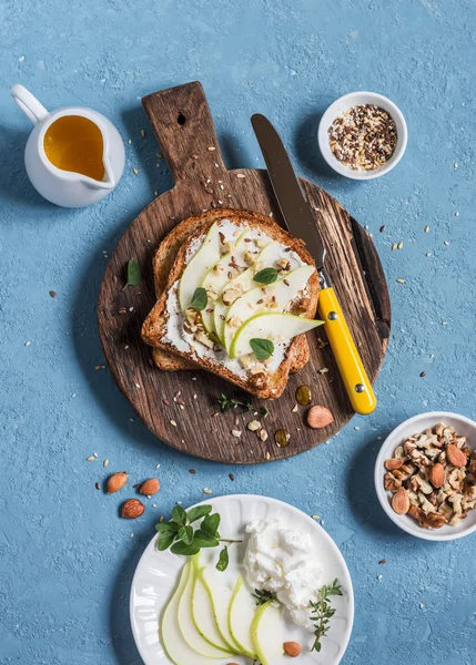 Toast with cheese, pear, honey and nuts. Delicious breakfast or snack on a blue background, top view.