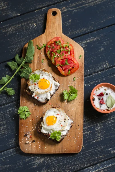 Toast with feta cheese and fried quail egg, fresh tomatoes on a dark wooden surface