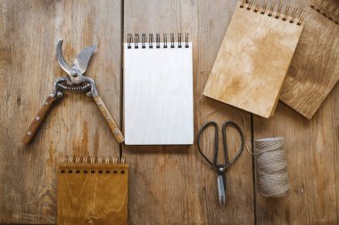 Bir masanın üzerinde klasik makas, budama defteri ve bir makara iplik vardır.