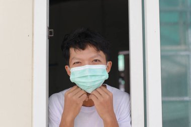 A masked man sticks his face out of a window while quarantined for 14 days.