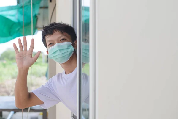 Asian man wearing a mask sticks his face out of the window while waving goodbye, copy specs.