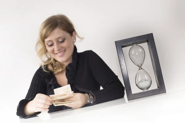 Manager counts banknotes earned with an houglass on the desk — Stock Photo, Image