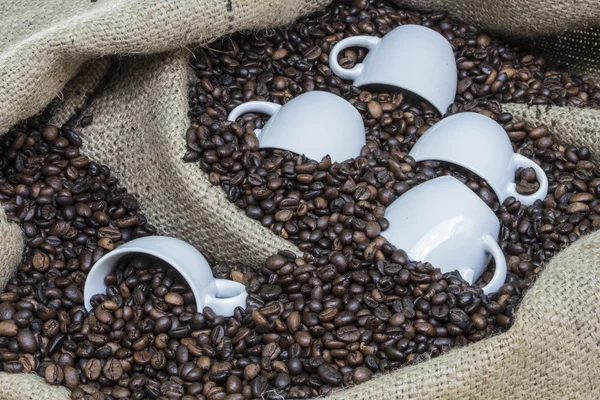 Tazas en un saco de arpillera lleno de granos de café —  Fotos de Stock