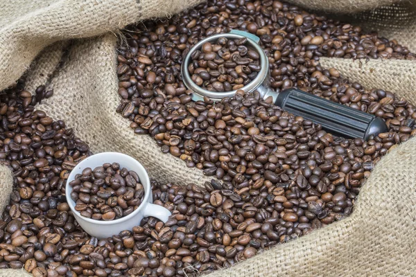 arm of coffee machine and cup in a burlap sack full of coffee beans