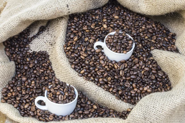 Чашки, полные кофейных зерен в мешочке с кофейными зёрнами — стоковое фото