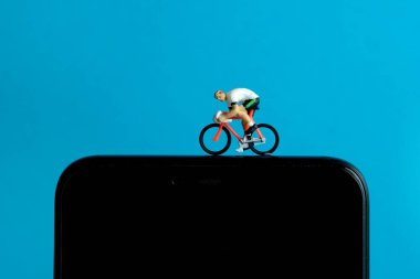 Bisiklet eğitmeni ve izleme uygulaması. Akıllı telefonun üstünde bir bisiklet. Minyatür insanlar kavramsal fotoğrafçılığı şekillendirir.