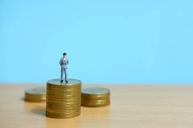 Parayı korumak için para yığınının üzerinde duran bir polis. Minyatür insanlar kavramsal fotoğrafçılığı şekillendirir.