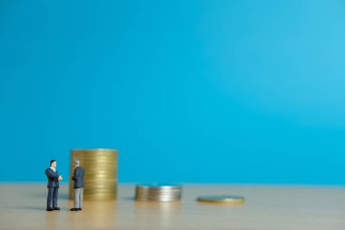 Minyatür iş konsepti - iki işadamı madeni para yığınının önünde ortaklık anlaşması için tokalaştı