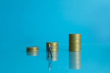 Minyatür iş konsepti. Parlak zemindeki madeni para yığını merdivenlerinin önünde duran bir iş adamı.