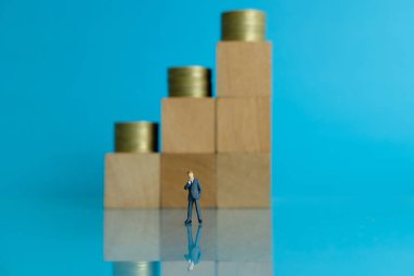 Minyatür iş konsepti - genç iş adamının para yığını grafiğiyle tahta bloğun önünde durması