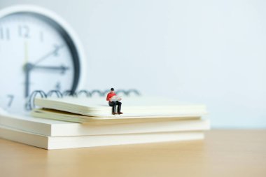 Sabah kitap okuma konsepti için minyatür insanlar. Kitap yığınının üzerinde oturan genç adam gazete okuyor.