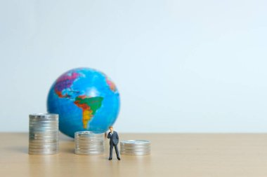 Minyatür iş konsepti. Para yığını ve dünyanın önünde düşünen bir iş adamı.