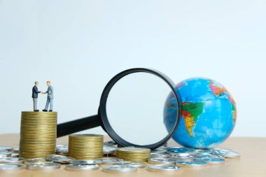 Minyatür insan iş konsepti. İki iş adamı, madeni para ve dünya üzerinde küresel ticaret ortaklığı konusunda anlaşma yaptı.