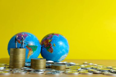 Minyatür insan iş konsepti. İki iş adamı, madeni para ve dünya üzerinde küresel ticaret ortaklığı konusunda anlaşma yaptı.