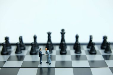 Minyatür iş konsepti - iki işadamı satranç piyonu önünde el sıkışma anlaşması yaptı