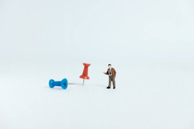 Minyatür iş konsepti - kırmızı ve mavi raptiye / raptiye yanında duran bir işadamı beyaz arkaplan
