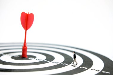 İş stratejisi kavramsal fotoğrafı - Minyatür işadamı dart tahtasının ortasında kırmızı oka doğru yürüyor