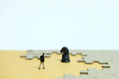 İş stratejisi kavramsal fotoğrafı - Minyatür işadamı yapbozun ortasında at şövalyesi piyonuna çarpıyor