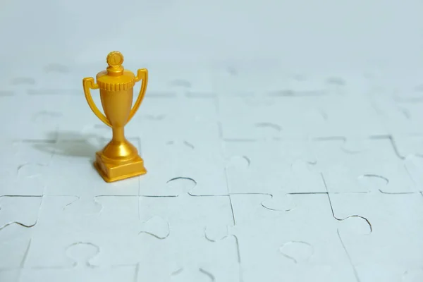 a golden trophy stands between a pile of puzzles