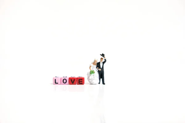 Miniature people photography. Bride and groom with love word beads on shiny white background
