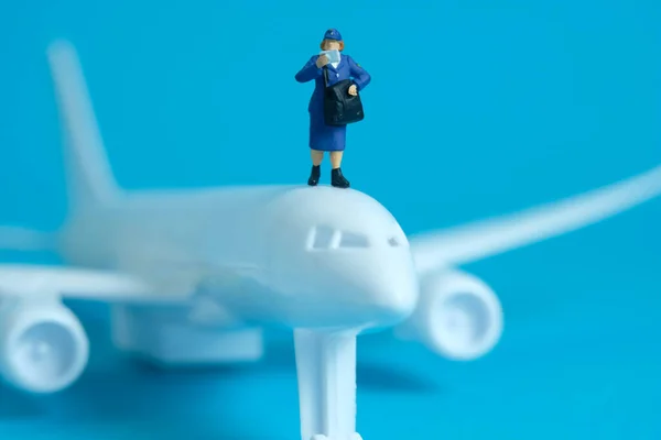 Miniature people toys conceptual photography. Airplane parcel package delivery. Postman courier with white plane, isolated on blue background.