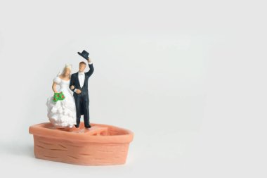 Gelin ve damat evlenmiş minyatür insanlar, beyaz bir arka planda izole bir şekilde, düğünden sonra teknenin üstünde duruyorlar. Resim fotoğrafı.