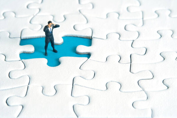 Бизнесмены, стоящие над пропавшей головоломкой, используют бинокль. Миниатюрные крошечные люди игрушки фотографии.