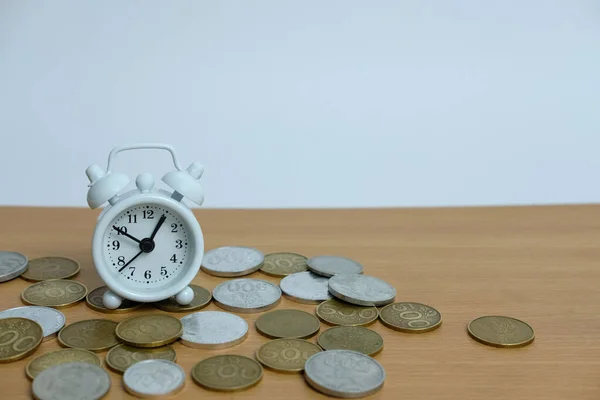 time is money concept - pile of money with white clock on a wooden table