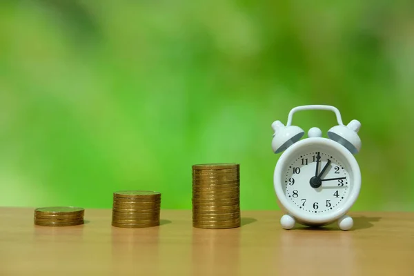 time is money concept - pile of money with white clock on a wooden table