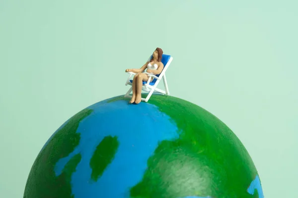 Miniature people toy figure photography. Travel destination concept, girl relaxing at beach chair above earth globe. Image photo