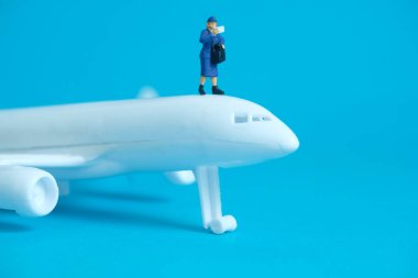 Minyatür insanlar kavramsal fotoğrafçılık oyuncakları. Uçak paketi teslimatı. Beyaz uçaklı postacı kuryesi, mavi arka planda izole edilmiş..