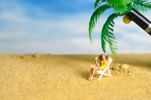 Miniature people toy figure photography. A girl relaxing on beach chair drinking a soft drink under the coconut tree. Image photo