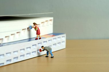 Minyatür insanlar oyuncak fotoğrafçılık. Kitap rafı konsepti. Bir grup öğrenci geri dönüyor ve bir kitap ödünç alıyorlar. Resim fotoğrafı.