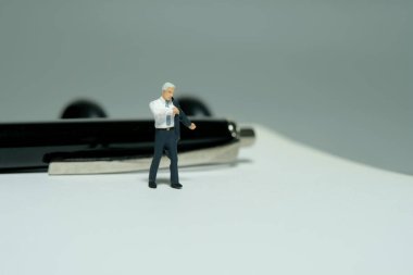 Minyatür minyatür insanlar oyuncak figürlü fotoğrafçılık. Kalem ve defterin önünde takım elbise giyen bir işadamı. Gri arka plan. Resim fotoğrafı.