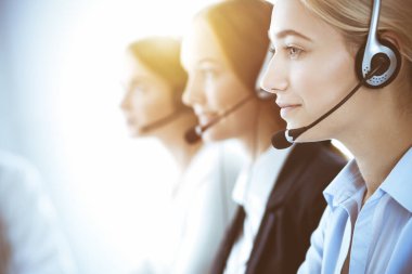 Çağrı merkezi ve iş adamları konsepti. Kulaklıklı, müşterilere danışan güzel bir iş kadını. Ofiste çalışan çeşitli telefon operatörleri