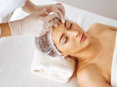 Güzellik uzmanı, genç esmer kadının yüzüne şırıngayla güzellik prosedürü uyguluyor. Kozmetik ilaç ve ameliyat, güzellik iğneleri.