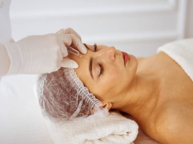 Güzellik uzmanı, genç esmer kadının yüzüne şırıngayla güzellik prosedürü uyguluyor. Kozmetik ilaç ve ameliyat, güzellik iğneleri.