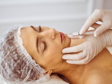 Güzellik uzmanı, genç esmer kadının yüzüne şırıngayla güzellik prosedürü uyguluyor. Kozmetik ilaç ve ameliyat, güzellik iğneleri.