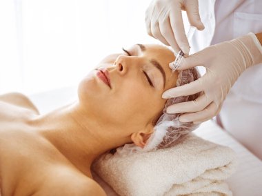 Güzellik uzmanı, genç esmer kadının yüzüne şırıngayla güzellik prosedürü uyguluyor. Kozmetik ilaç ve ameliyat, güzellik iğneleri.