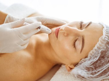 Güzellik uzmanı, genç esmer kadının yüzüne şırıngayla güzellik prosedürü uyguluyor. Kozmetik ilaç ve ameliyat, güzellik iğneleri.