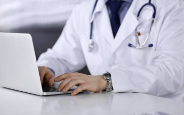 Bilinmeyen bir erkek doktor klinikte dizüstü bilgisayarla yakın planda çalışıyor. İşteki genç doktor. Mükemmel sağlık hizmeti, tıp konsepti