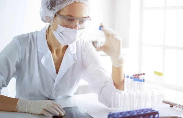 Cientista profissional em óculos de proteção pesquisando tubo com reagentes em laboratório ensolarado. Medicina e investigação científica — Fotografia de Stock