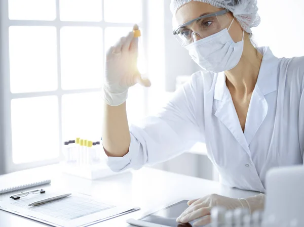Científica profesional en gafas protectoras investigando tubo con reactivos en laboratorio soleado. Investigación en medicina y ciencia — Foto de Stock